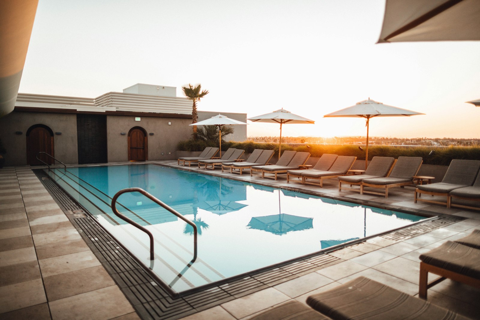 Outdoor swimming pool with handrail, tiled coping and loungers at sunset